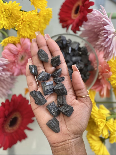 Raw Black Tourmaline stone held in hand over a bowl of Raw Black Tourmaline. Raw Black Tourmaline provides protection, including EMF protection.